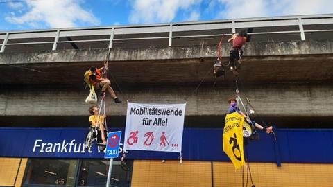Vier Personen hängen an Kletterseilen, zwei davon in Rollstühlen, am Bahnhof Frankfurt West