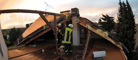 Feuerwehrleute arbeiten am Dachstuhl eines beschädigten Hauses