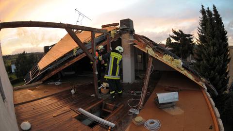 Feuerwehrleute arbeiten am Dachstuhl eines beschädigten Hauses