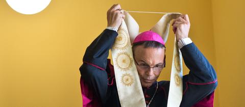 Ein Bischof zieht seine Arbeitskleidung über.