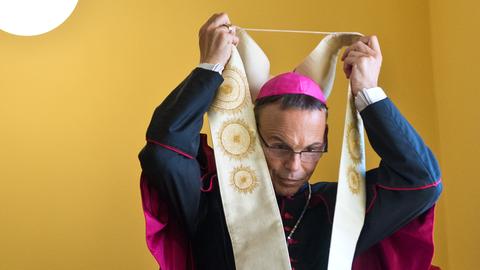 Ein Bischof zieht seine Arbeitskleidung über.