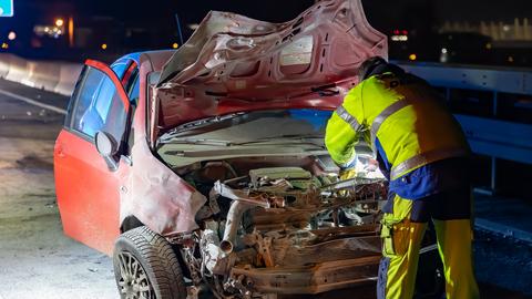 Ausgebranntes Auto, davor ein Mann in Warnkleidung von hinten