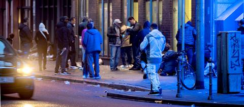 Menschen stehen am Abend im Frankfurter Bahnhofsviertels vor einem Drogenkonsumraum. 