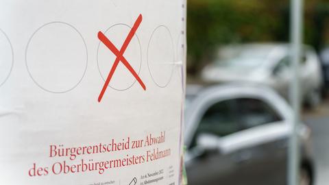 Ein weißes Plakat mit rotem Kreuz weist auf den anstehenden Bürgerentscheid zur Abwahl des Oberbürgermeisters Feldmann (SPD) hin. 