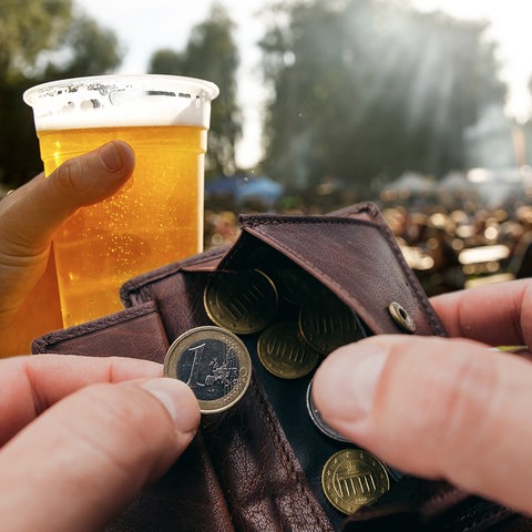 Im Vordergrund eine Geldbörse mit Kleingeld, im Hintergrund ein Volksfest