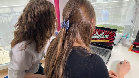 Zwei Schülerinnen von hinten vor einem Laptop mit der Webseite "Der Fabulant" geöffnet.
