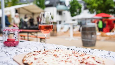 Ein Flammkuchen und ein stehen auf einem Tisch. Im Hintergrund zeigt sich eine Volksfest-Atmosphäre