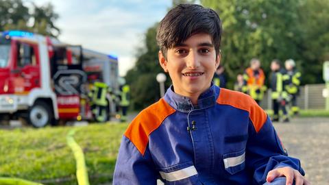 Siwar hockt neben dem Löschschlauch vor dem roten Einsatzfahrzeug.