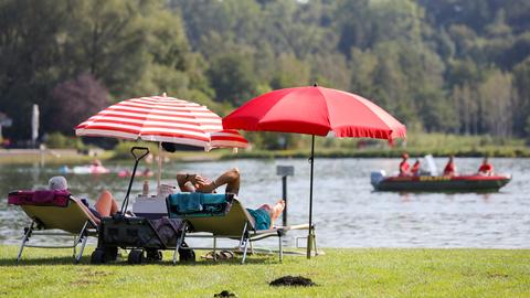 Zwei Menschen auf Sonnenliegen mit Sonnenschirm am Badesee im Sommer