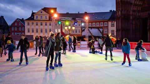 Jugendliche laufen Schlittschuh auf einer Eisbahn mit bunten Lichtern.