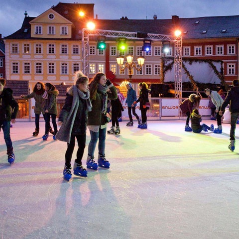 Jugendliche laufen Schlittschuh auf einer Eisbahn mit bunten Lichtern.