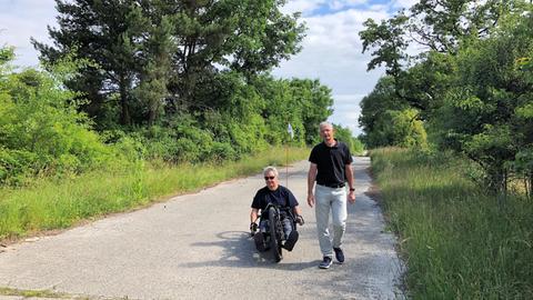 Zwei Männer auf einem Weg durch den Wald, einer laufend, der andere mit dem Handbike fahrend