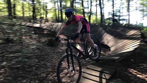 Ein Mensch auf einem Fahrrad im Wald, fährt über Holzrampen