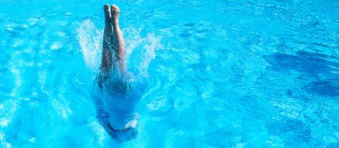 Eine Frau taucht in ein leeres Schwimmbecken ein. Nur noch ihre Füße sind zu sehen.