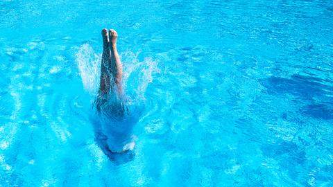 Eine Frau taucht in ein leeres Schwimmbecken ein. Nur noch ihre Füße sind zu sehen.