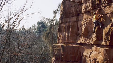 Eine Sandsteinwand, daran ist ein Kletterer befestigt, der in großen Höhen klettern.