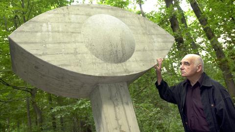 Karl Oskar Blase steht neben einem Beton-Auge, einem Grabstein.