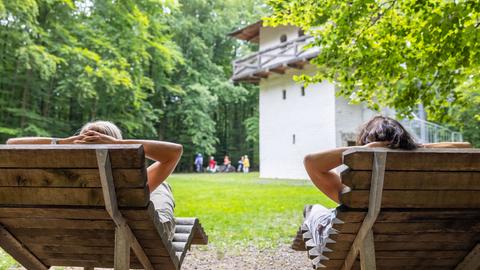 Zwei Menschen liegen auf Liegestühlen vor einem römischen Wachtturm.