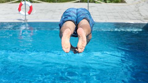 Mann springt kopfüberin ein Schwimmbecken im Freibad
