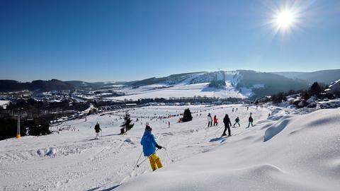 Mit Schnee bedeckte Landschaft bei strahlendem Sonnenschein. Menschen fahren Ski.