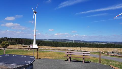 Ein Bergplateau, ein Windrad ist zu sehen - daneben steht eine Tafel mit römischen Zahlen - das sind die Uhrzeiten der Sonnenuhr.