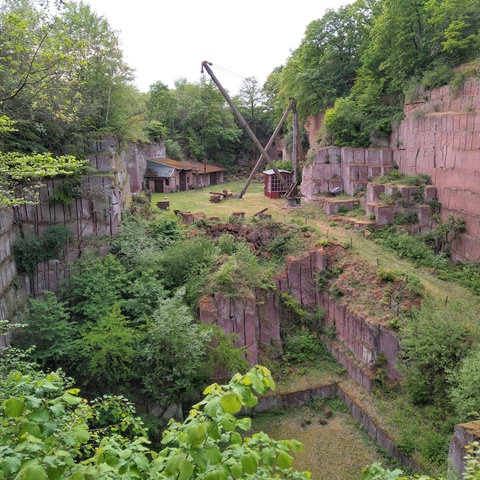 Der Steinbruch Michelnau, eine Art Grube, die von roten Steinen umrandet ist - im Hintergrund steht ein Holzkran.