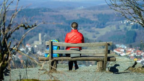 Frau sitzt auf einer Bank und blickt auf die Burg Reifenberg