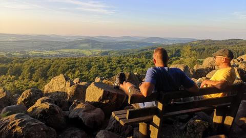 zwei Wanderer blicken vom Schafstein am Wanderweg "Der Ehrenberger" in die Rhön