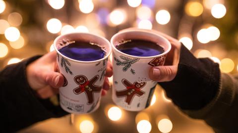 Zwei Hände, die mit Glühwein gefüllten Bechern auf dem Weihnachtsmarkt anstoßen.