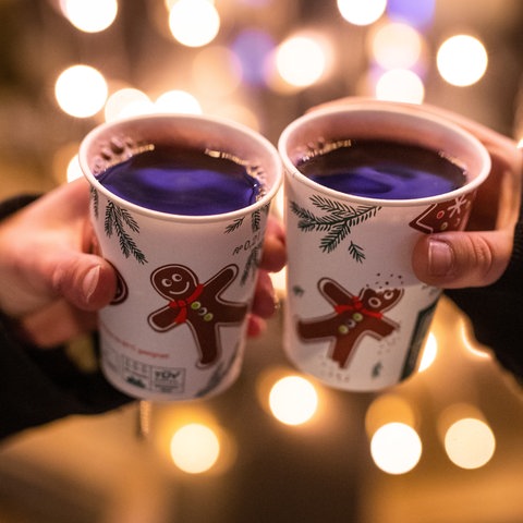 Zwei Hände, die mit Glühwein gefüllten Bechern auf dem Weihnachtsmarkt anstoßen.