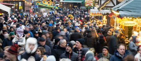 Viele Besucherinnen und Besucher strömen zwischen den Verkaufs- und Imbissständen auf dem Weihnachtsmarkt in Frankfurt hindurch. 