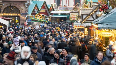 Viele Besucherinnen und Besucher strömen zwischen den Verkaufs- und Imbissständen auf dem Weihnachtsmarkt in Frankfurt hindurch. 