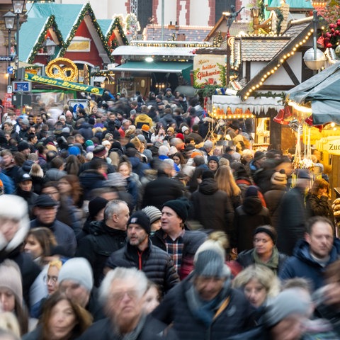 Viele Besucherinnen und Besucher strömen zwischen den Verkaufs- und Imbissständen auf dem Weihnachtsmarkt in Frankfurt hindurch. 