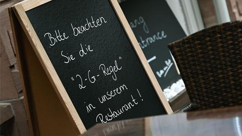 Eine Tafel in einem Restaurant-Interieur. Darauf steht mit Kreide geschrieben "Bitte beachten Sie die 2-G-Regel in unserem Restaurant".