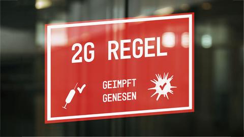 Eine rotes Schild an einer Glastür. Darauf steht geschrieben "2G Regel - Geimpft, Genesen". Und daneben Symbole für ein Coronavirus und eine Spritze.