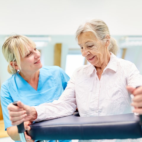 Eine Altenpflegerin übt mit einer Seniorin in einem Turnraum