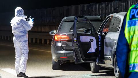 Eine Person in weißem Schutzanzug fotografiert zwei leere Autos am Rand einer Autobahn.