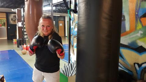 Sozialarbeiterin Antje Heigl steht mit Boxhandschuhen in einer Sporthalle neben einem Boxsack