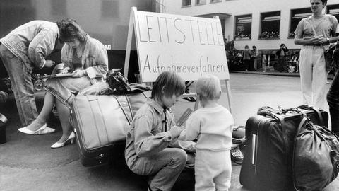 S/W-Foto: Frauen und Kinder mit viel Gepäck. In ihrer Mitte ein Schild mit der Aufschrift "Leitstelle Aufnahmeverfahren".