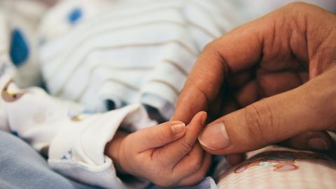 Ein Neugeborenes, dessen Hand von einer Hebamme gehalten wird