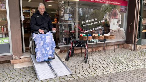 Rollstuhlfahrer auf Klapprampe vor Geschäft