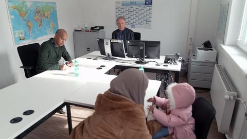 Peter Gärtner sitzt an einem Schreibtisch, neben ihm ein Übersetzer und vor dem Tisch eine junge Somalierin mit Kopftuch und ihrer kleinen Tochter