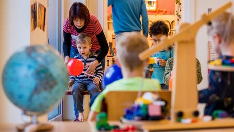 Kinder spielen mit Bauklötzen, eine Frau ist bei ihnen. 