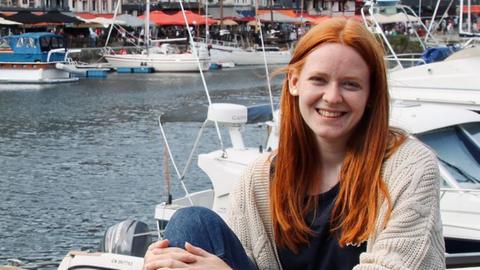 Stella Berker sitzt auf einer Mauer an einem Hafen