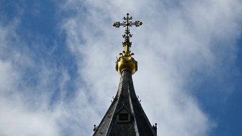 Das Bild zeigt ein goldenes Kreuz auf dem Turm des Mittelbaus des Mainzer Doms vor einem blauen Himmel.