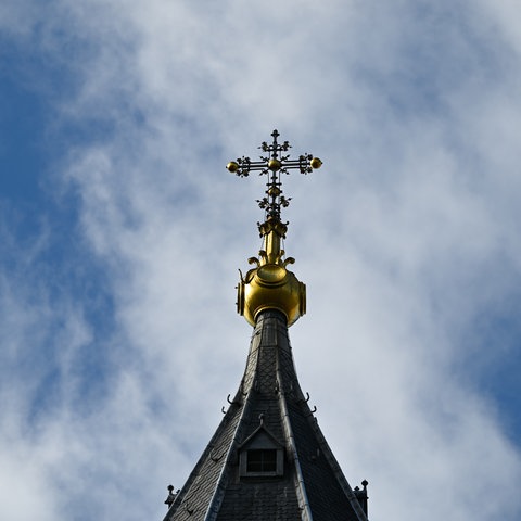 Das Bild zeigt ein goldenes Kreuz auf dem Turm des Mittelbaus des Mainzer Doms vor einem blauen Himmel.