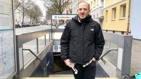 Ein Mann mit Sehbehinderung steht am Treppenabgang zu einer U-Bahn. Er hält einen "Blindenstock" zusammengeklappt in seiner Hand.