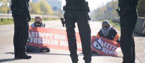 Aktivisten sitzen mit Transparent auf der A66, davor stehen Polizisten.