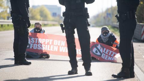 Aktivisten sitzen mit Transparent auf der A66, davor stehen Polizisten.