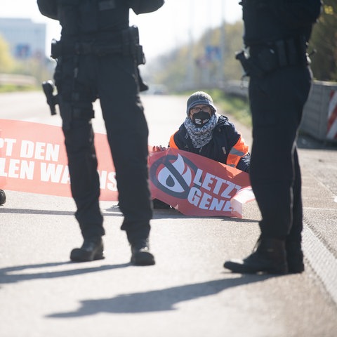 Aktivisten sitzen mit Transparent auf der A66, davor stehen Polizisten.